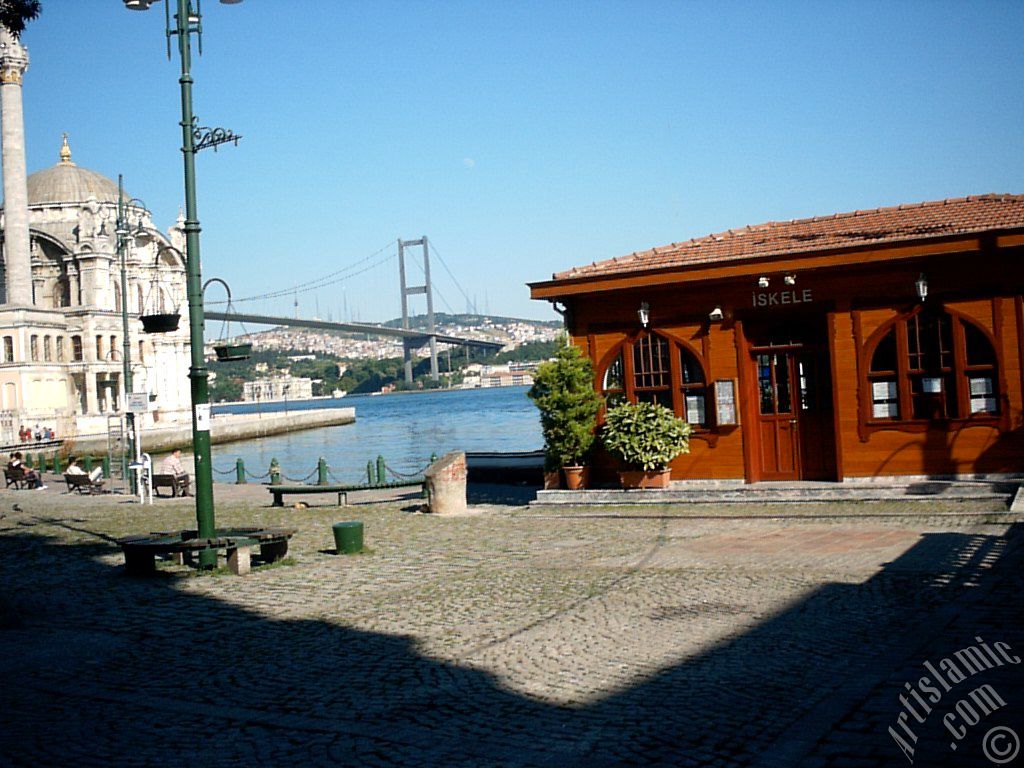 View of the jetty, Bosphorus Bridge, Ortakoy Mosque and the moon seen in daytime over the bridge`s legs from Ortakoy shore in Istanbul city of Turkey.
