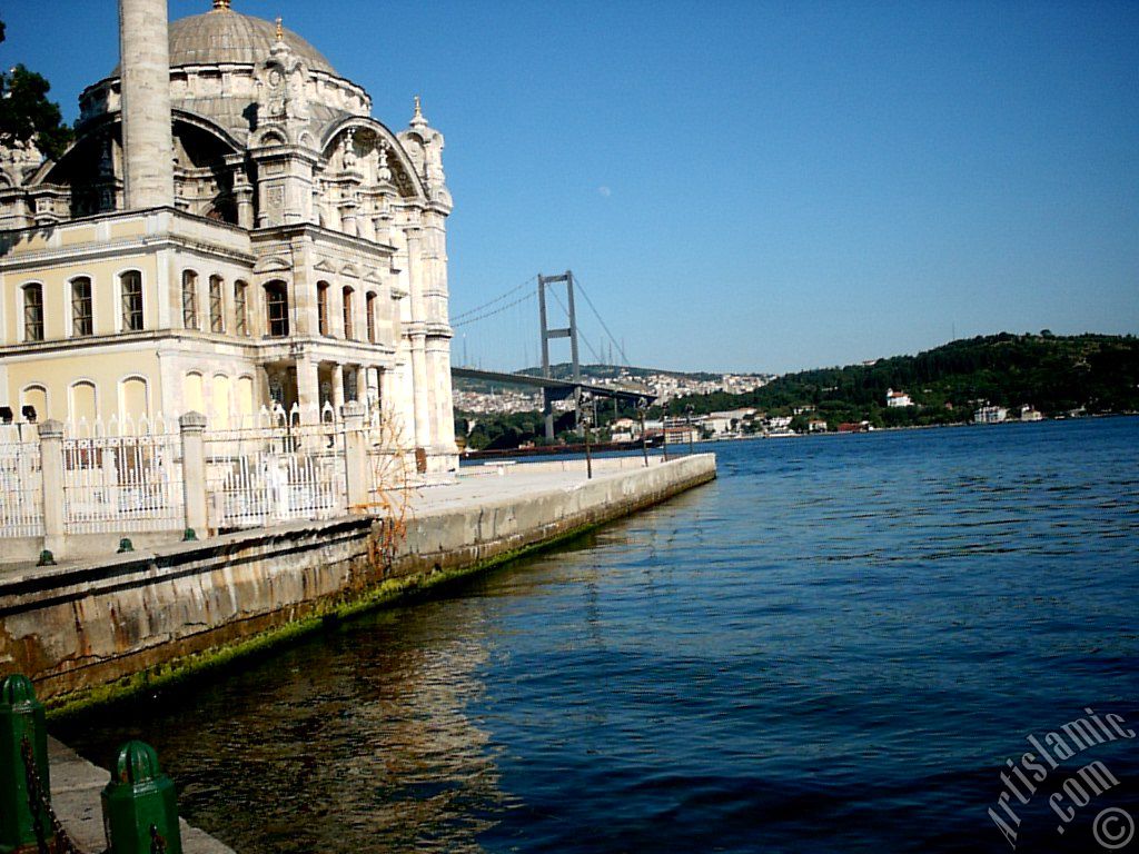 View of Bosphorus Bridge, Ortakoy Mosque and the moon seen in daytime over the bridge`s legs from Ortakoy shore in Istanbul city of Turkey.
