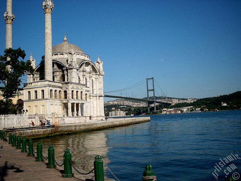 View of Bosphorus Bridge, Ortakoy Mosque and the moon seen in daytime over the bridge`s legs from Ortakoy shore in Istanbul city of Turkey.
