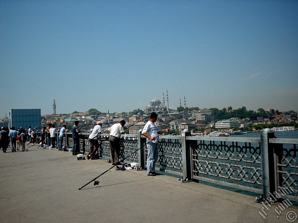 View of fishing people, on the horizon Beyazit Tower and Suleymaniye Mosque from Galata Bridge located in Istanbul city of Turkey.
