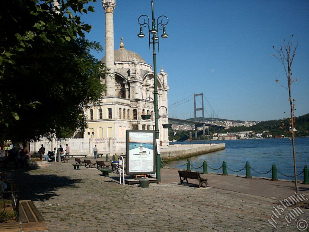 View of Bosphorus Bridge, Ortakoy Mosque and the moon seen in daytime over the bridge`s legs from Ortakoy shore in Istanbul city of Turkey.
