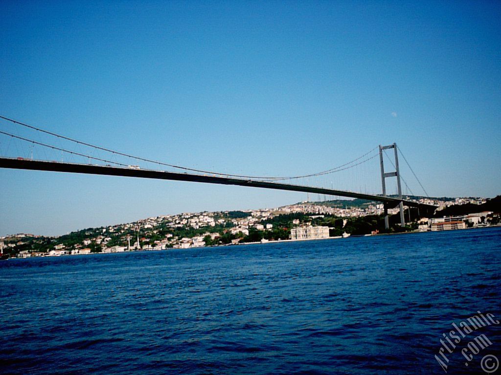 View of Bosphorus Bridge, Camlica Hill, Beylerbeyi coast and the moon seen in daytime over the bridge`s legs from Ortakoy shore in Istanbul city of Turkey.
